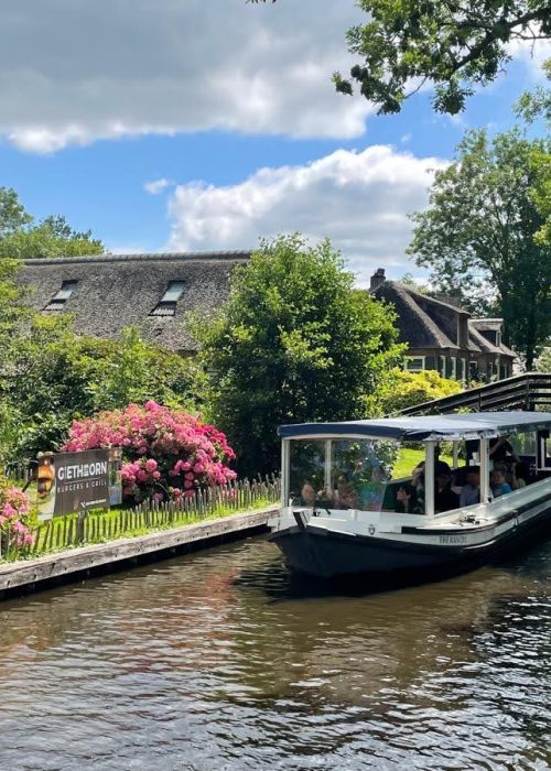 Electric boat cruising past thatched cottage on Giethoorn canal